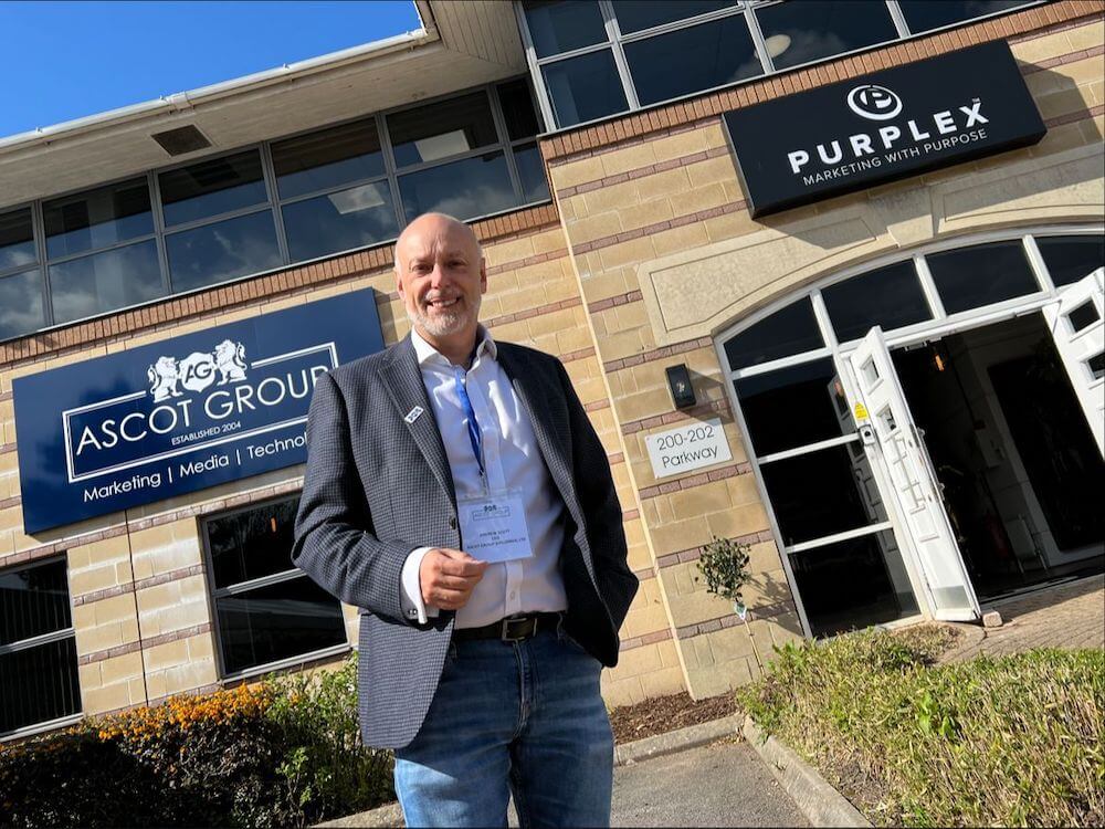 Andrew Scott stands outside the Purplex Marketing and Ascot Group headquarters on a sunny day, smiling confidently in a business-casual outfit.